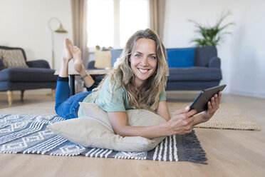 Portrait of smiling woman lying on the floor at home using tablet - SBOF01909