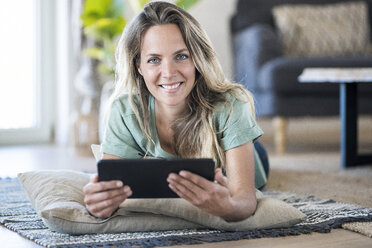 Porträt einer lächelnden Frau, die zu Hause auf dem Boden liegt und ein Tablet benutzt - SBOF01910