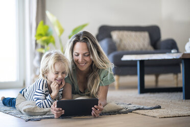 Lächelnde Mutter und Sohn liegen zu Hause auf dem Boden und benutzen ein Tablet - SBOF01911