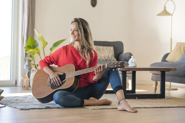 Lächelnde Frau, die zu Hause auf dem Boden sitzt und Gitarre spielt - SBOF01922