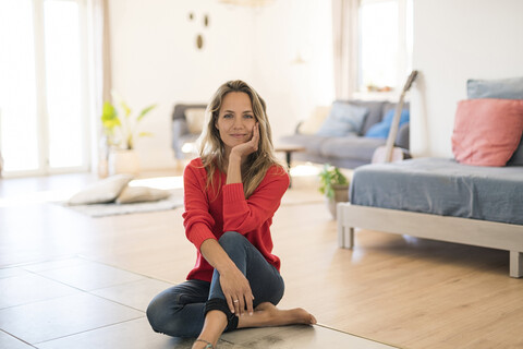 Porträt einer lächelnden Frau, die zu Hause auf dem Boden sitzt, lizenzfreies Stockfoto