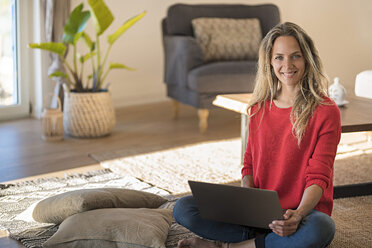 Porträt einer lächelnden Frau, die zu Hause auf dem Boden sitzt und einen Laptop benutzt - SBOF01929