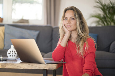 Nachdenkliche Frau mit Laptop auf dem Couchtisch zu Hause - SBOF01932