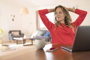 Frau sitzt am Esstisch zu Hause und macht eine Pause von ihrer Arbeit am Laptop - SBOF01934