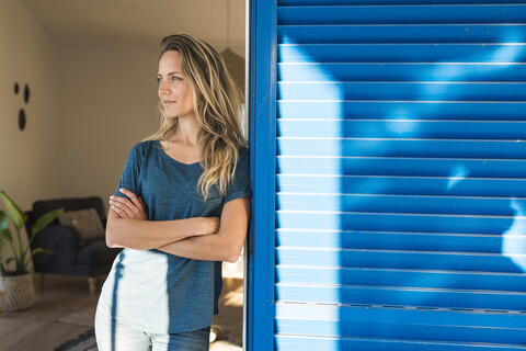 Frau lehnt an offenem Fenster zu Hause und schaut zur Seite, lizenzfreies Stockfoto