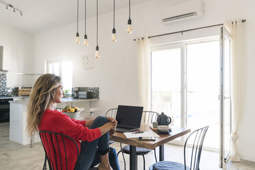 Woman using laptop on dining table in modern home - SBOF01957