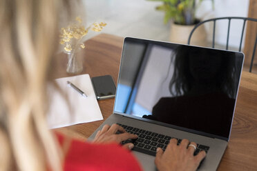 Close-up of woman using laptop on wooden table at home - SBOF01959