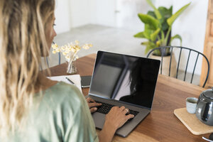 Nahaufnahme einer Frau, die einen Laptop auf einem Holztisch zu Hause benutzt - SBOF01960