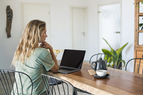 Woman using laptop on dining table at home stock photo