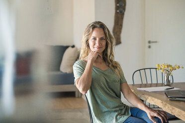 Portrait of smiling woman with laptop sitting at dining table at home - SBOF01963