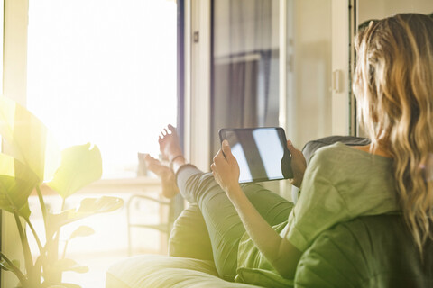 Woman relaxing in armchair at home holding tablet stock photo