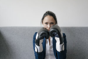 Porträt einer jungen Frau auf einer Couch mit Boxhandschuhen - KNSF05731