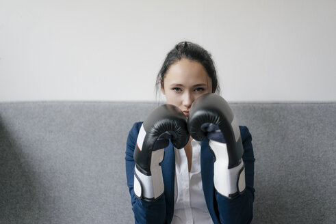 Portrait of young woman on couch wearing boxing gloves - KNSF05731
