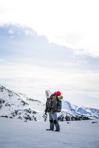 Junger Mann mit Rucksack, schneebedeckte Berge im Hintergrund, lizenzfreies Stockfoto