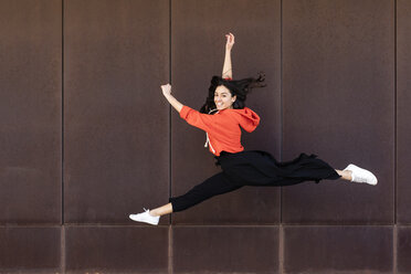 Young contemporary dancer in front of a rusty wall jumping and dancing, looking at camera - JRFF02855