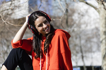 Young contemporary dancer wearing red hoodie shirt, sitting and listening to music - JRFF02874