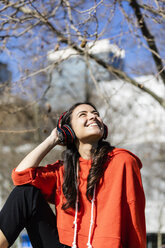 Young contemporary dancer wearing red hoodie shirt, sitting and listening to music - JRFF02875