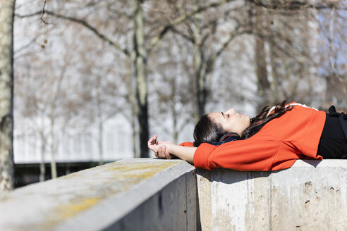 Young contemporary dancer wearing red hoodie shirt, lying and listening to music - JRFF02876