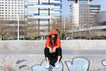 Junge zeitgenössische Tänzerin mit rotem Kapuzen-Shirt, auf dem Boden sitzend, mit der Stadt im Hintergrund - JRFF02877