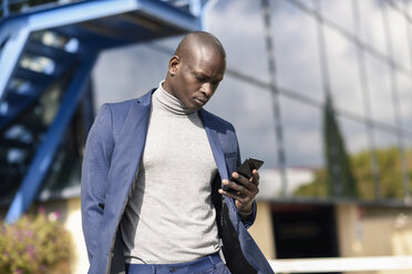 Geschäftsmann in blauem Anzug und grauem Rollkragenpullover schaut auf sein Handy - JSMF00877
