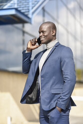 Porträt eines lächelnden Geschäftsmannes im blauen Anzug am Telefon - JSMF00880