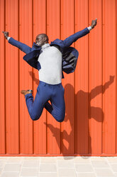 Erfolgreicher Geschäftsmann, der vor einer orangefarbenen Wand in die Luft springt - JSMF00898
