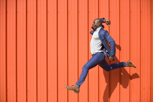 Geschäftsmann, der vor einer orangefarbenen Wand in die Luft springt - JSMF00900