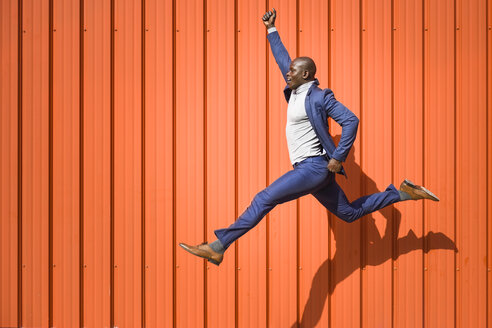 Businessman jumping in the air in front of orange wall - JSMF00901