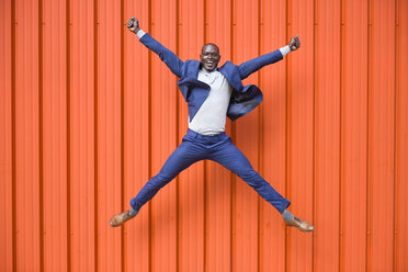 Happy businessman jumping in the air in front of orange wall - JSMF00903
