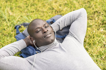 Porträt eines Geschäftsmannes, der auf einer Wiese liegt und mit Kopfhörern Musik hört - JSMF00910