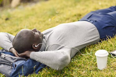 Businessman lying on a meadow listening music with earphones - JSMF00913