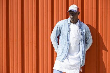 Man wearing casual denim clothes and cap standing in front of orange wall - JSMF00924