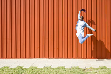 Man wearing casual denim clothes jumping in the air in front of orange wall - JSMF00925