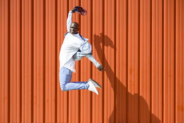 Man wearing casual denim clothes jumping in the air in front of orange wall - JSMF00926