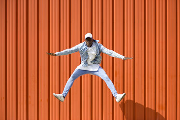 Man wearing casual denim clothes jumping in the air in front of orange wall - JSMF00927