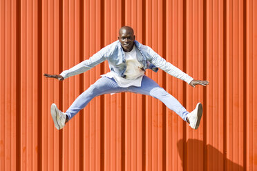 Man wearing casual denim clothes jumping in the air in front of orange wall - JSMF00929