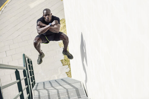 Mann in schwarzer Sportkleidung springt auf einer Treppe in die Luft - JSMF00942