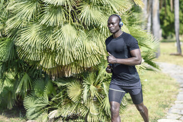 Spain, man in black sportswear running in a park listening music with wireless headphones - JSMF00949