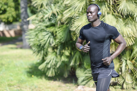 Spain man in black sportswear running in a park listening music