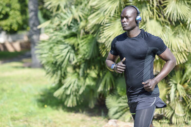 Spain, man in black sportswear running in a park listening music with wireless headphones - JSMF00950