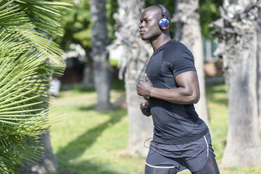 Spain, man in black sportswear running in a park listening music with wireless headphones - JSMF00951