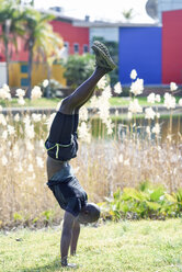 Mann in schwarzer Sportkleidung macht Handstand auf einer Wiese - JSMF00955