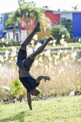 Mann in schwarzer Sportkleidung macht einhändigen Handstand auf einer Wiese - JSMF00956