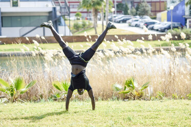 Mann in schwarzer Sportkleidung macht Handstand auf einer Wiese - JSMF00957