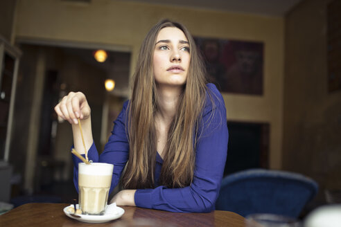 Junge Frau sitzt am Tisch in einem Café und schaut zur Seite - PNEF01315