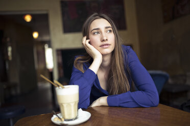 Junge Frau sitzt am Tisch in einem Café und schaut zur Seite - PNEF01317