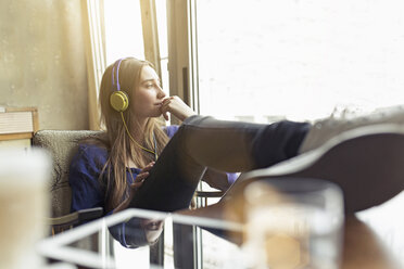 Relaxed young woman sitting on a chair wearing headphones - PNEF01322