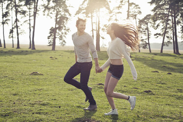 Happy young couple running hand in hand on meadow - PNEF01323