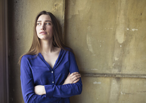 Junge Frau steht an einer Wand und schaut zur Seite, lizenzfreies Stockfoto