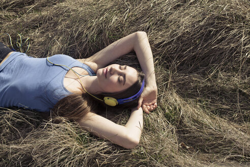 Entspannte junge Frau mit Kopfhörern auf einer Wiese liegend - PNEF01331